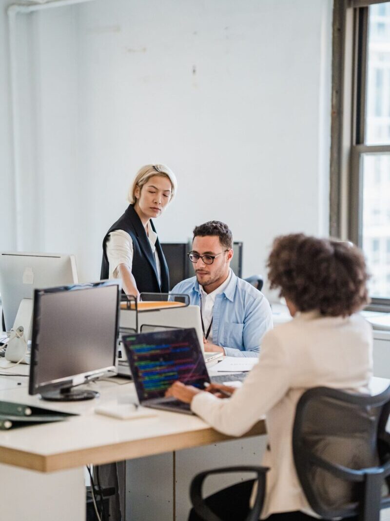 Business team working collaboratively in a modern office setting with computers and laptops.