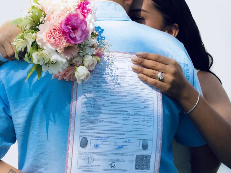 Couple embraces holding marriage certificate and flowers, symbolizing new beginnings.
